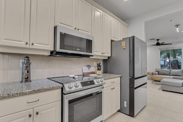 kitchen with appliances with stainless steel finishes, white cabinetry, backsplash, light stone counters, and ceiling fan