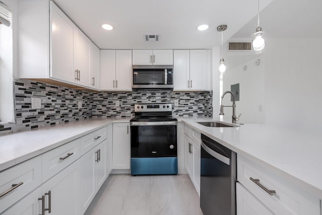 kitchen with appliances with stainless steel finishes, sink, pendant lighting, and white cabinets