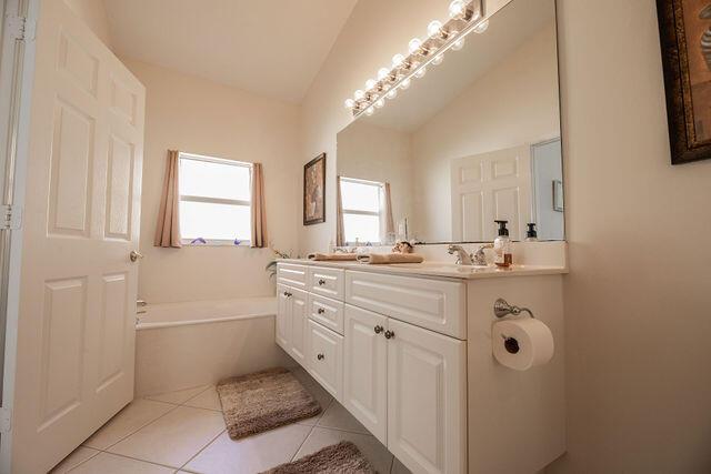 bathroom featuring a tub to relax in, tile patterned floors, vanity, and lofted ceiling