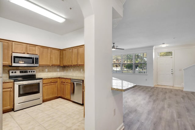 kitchen featuring kitchen peninsula, backsplash, ceiling fan, light stone counters, and stainless steel appliances