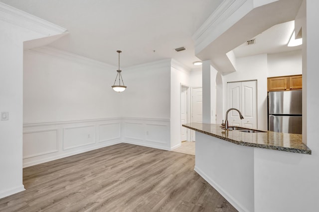kitchen featuring dark stone counters, a sink, ornamental molding, visible vents, and freestanding refrigerator
