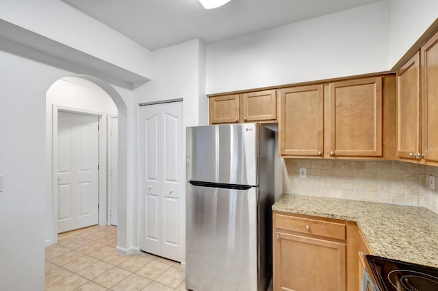 kitchen featuring decorative backsplash, light tile patterned flooring, arched walkways, stainless steel appliances, and light stone countertops