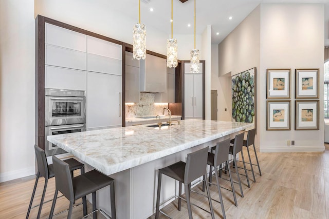 kitchen featuring sink, a breakfast bar, double oven, hanging light fixtures, and a center island with sink