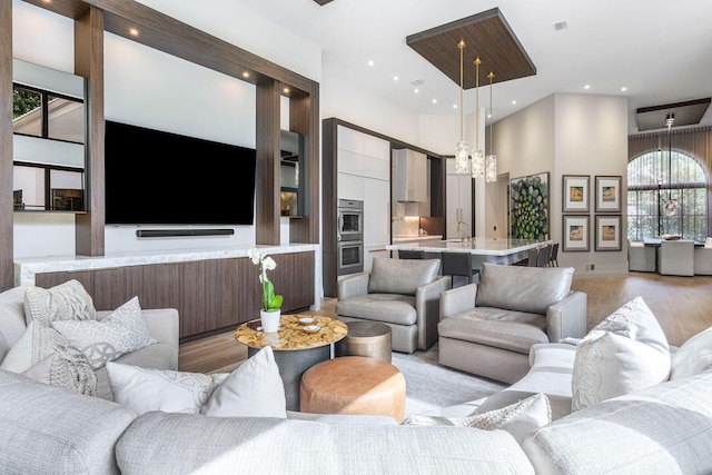 living room with an inviting chandelier, sink, a high ceiling, and light wood-type flooring