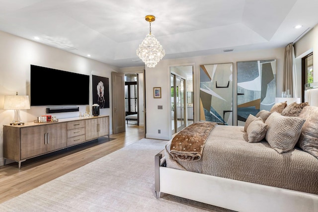 bedroom with a tray ceiling, light hardwood / wood-style floors, and a notable chandelier