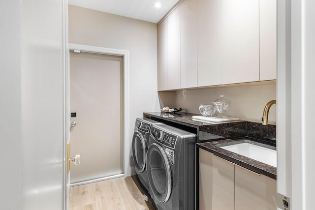 clothes washing area with cabinets, sink, light hardwood / wood-style floors, and washing machine and dryer