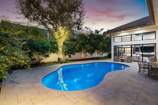 pool at dusk featuring a patio