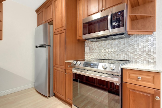 kitchen with stainless steel appliances, light wood-type flooring, light stone counters, and decorative backsplash