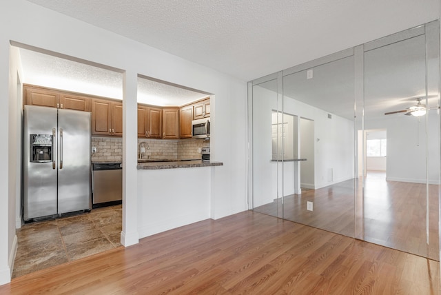 kitchen with ceiling fan, backsplash, stainless steel appliances, light hardwood / wood-style floors, and a textured ceiling