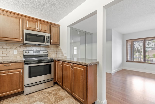 kitchen featuring light stone counters, a textured ceiling, appliances with stainless steel finishes, kitchen peninsula, and backsplash