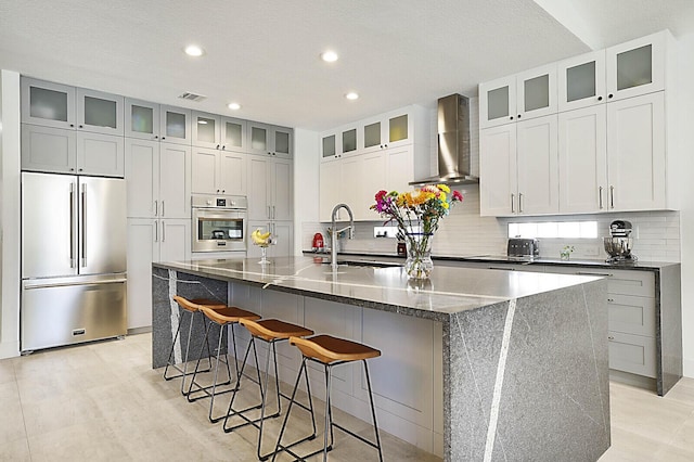 kitchen featuring stainless steel appliances, visible vents, backsplash, a sink, and wall chimney range hood