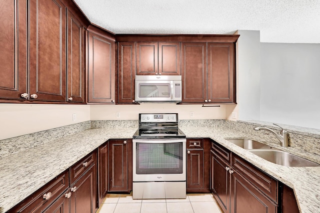 kitchen with sink, light tile patterned floors, appliances with stainless steel finishes, light stone counters, and a textured ceiling