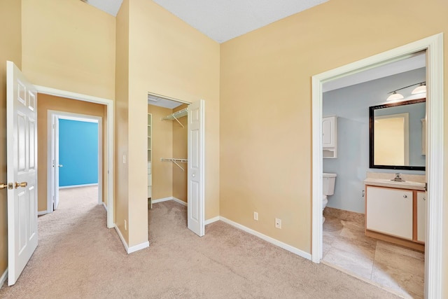 unfurnished bedroom featuring connected bathroom, sink, a walk in closet, light carpet, and a closet