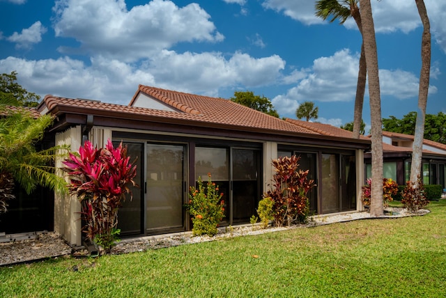 back of house with a yard, a sunroom, and a tiled roof