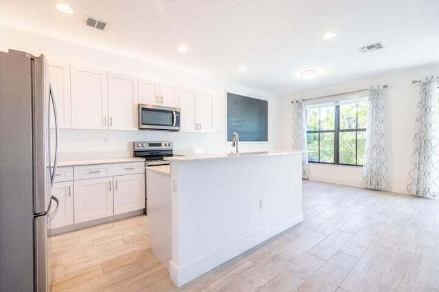 kitchen with stainless steel appliances, white cabinetry, sink, and a center island with sink