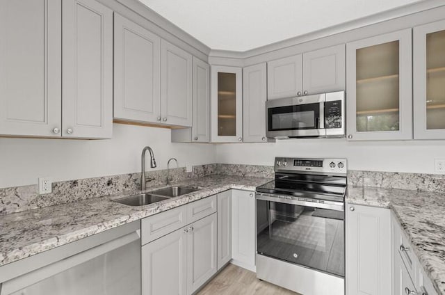 kitchen with sink, light hardwood / wood-style flooring, stainless steel appliances, light stone countertops, and white cabinets