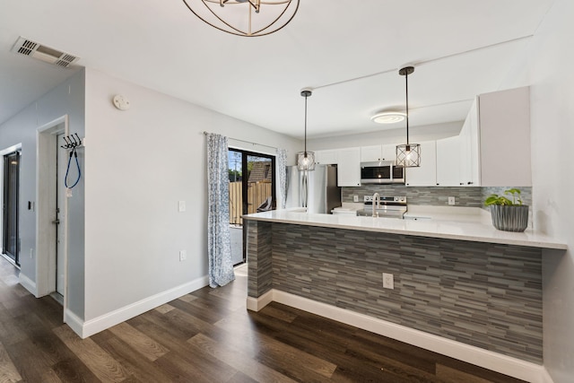 kitchen with dark wood-type flooring, appliances with stainless steel finishes, white cabinetry, tasteful backsplash, and kitchen peninsula