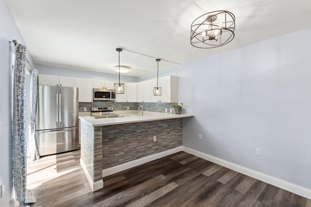 kitchen featuring appliances with stainless steel finishes, pendant lighting, white cabinets, decorative backsplash, and kitchen peninsula