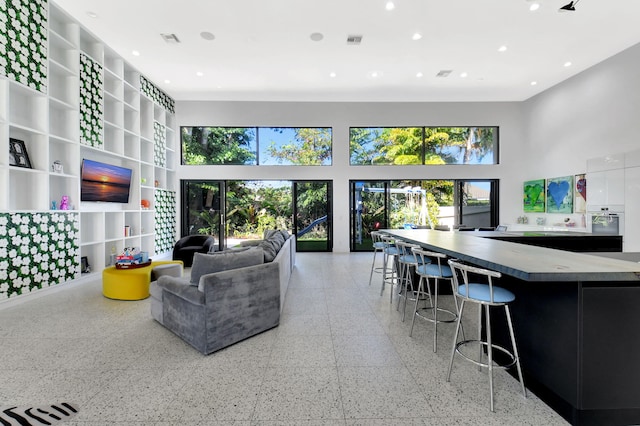 living area featuring light speckled floor, recessed lighting, a healthy amount of sunlight, and a towering ceiling