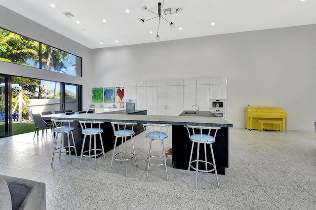 kitchen with light speckled floor, a towering ceiling, a kitchen bar, and white cabinetry