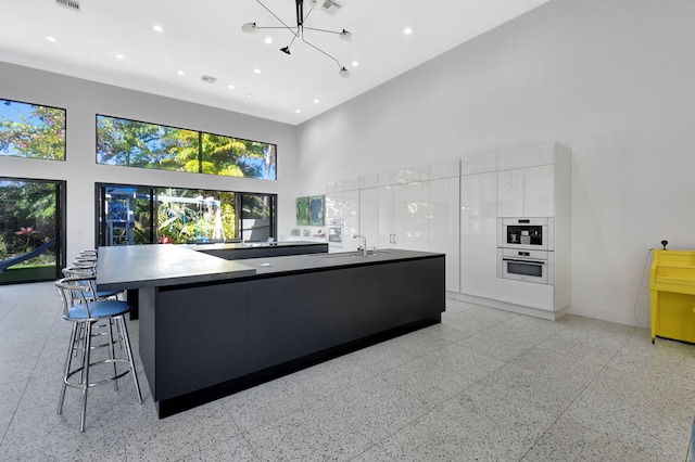 kitchen with light speckled floor, a high ceiling, white cabinets, a large island, and modern cabinets