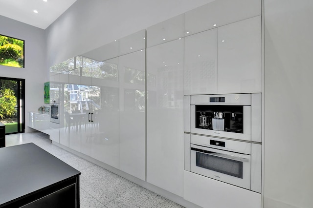 kitchen featuring a towering ceiling, modern cabinets, white cabinets, and light speckled floor