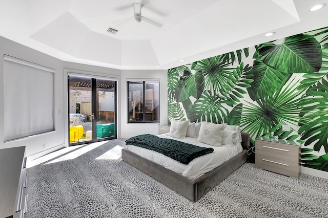 bedroom featuring light colored carpet, an accent wall, access to exterior, a tray ceiling, and recessed lighting