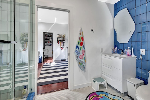 interior space featuring toilet, a tile shower, tile walls, and vanity