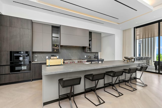 kitchen featuring a breakfast bar, tasteful backsplash, sink, a wall of windows, and light hardwood / wood-style flooring