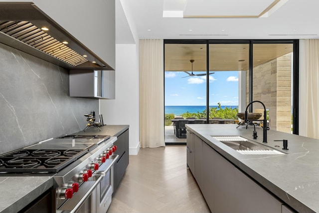 kitchen with sink, custom exhaust hood, a water view, tasteful backsplash, and range with two ovens