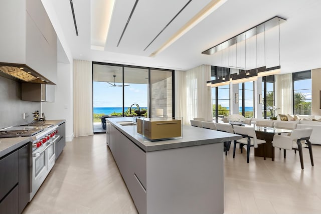 kitchen featuring sink, a wall of windows, double oven range, a water view, and a center island with sink