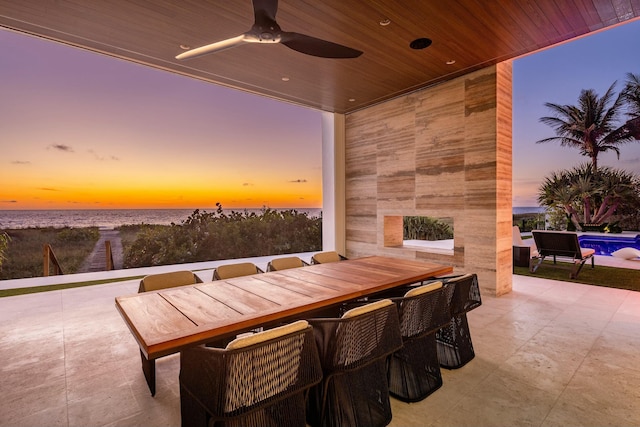 patio terrace at dusk featuring ceiling fan and a water view