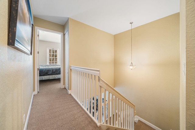 hallway featuring carpet floors, baseboards, a textured wall, and an upstairs landing