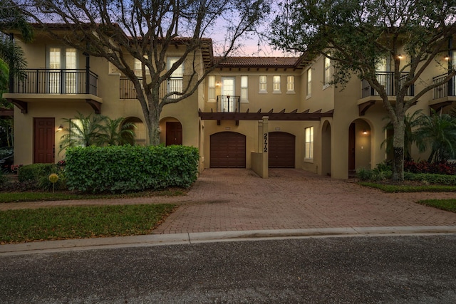 mediterranean / spanish house with a tile roof, stucco siding, an attached garage, a balcony, and driveway