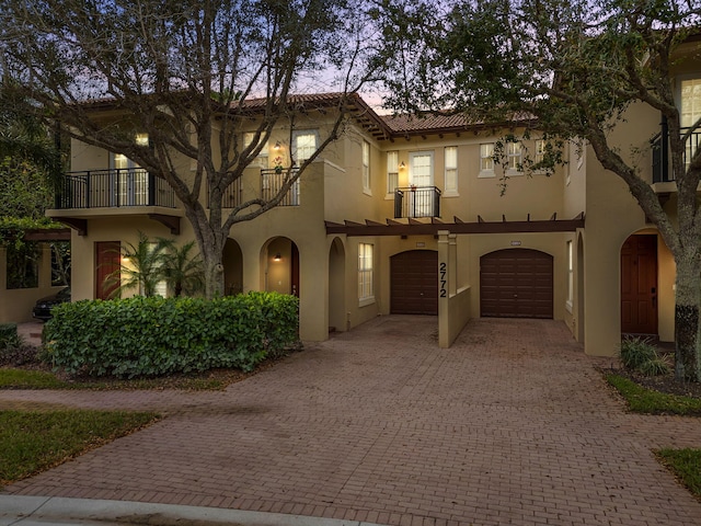 mediterranean / spanish house featuring a balcony, a garage, driveway, a tiled roof, and stucco siding