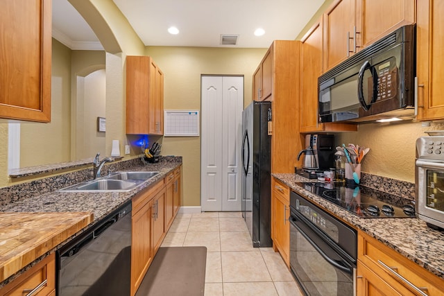 kitchen featuring visible vents, light tile patterned flooring, a sink, dark stone counters, and black appliances