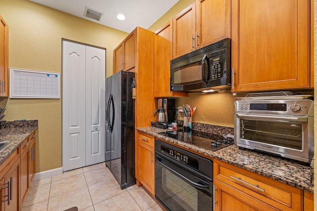 kitchen with light tile patterned flooring, visible vents, black appliances, brown cabinetry, and dark stone countertops