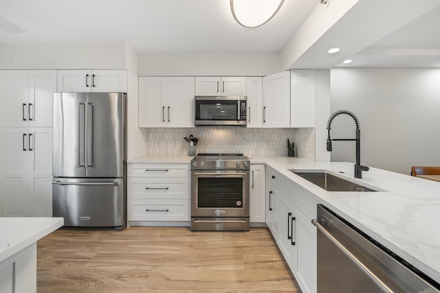 kitchen featuring sink, light hardwood / wood-style flooring, premium appliances, light stone countertops, and white cabinets