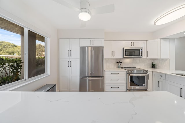 kitchen with tasteful backsplash, appliances with stainless steel finishes, light stone countertops, and white cabinets