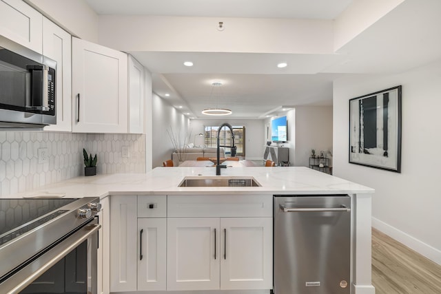 kitchen with appliances with stainless steel finishes, white cabinetry, sink, decorative backsplash, and light stone countertops