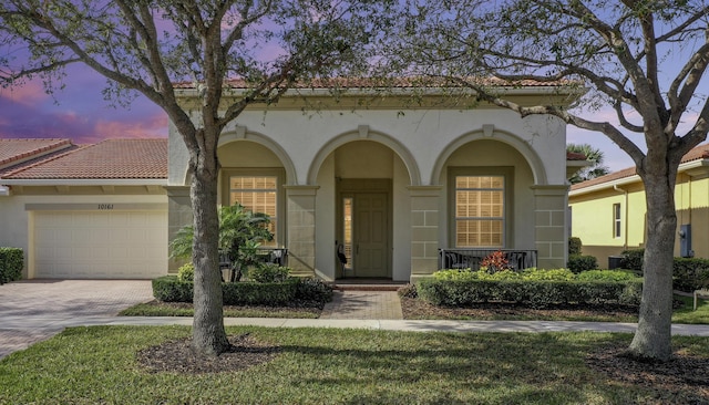 mediterranean / spanish house featuring a tile roof, decorative driveway, a garage, and stucco siding