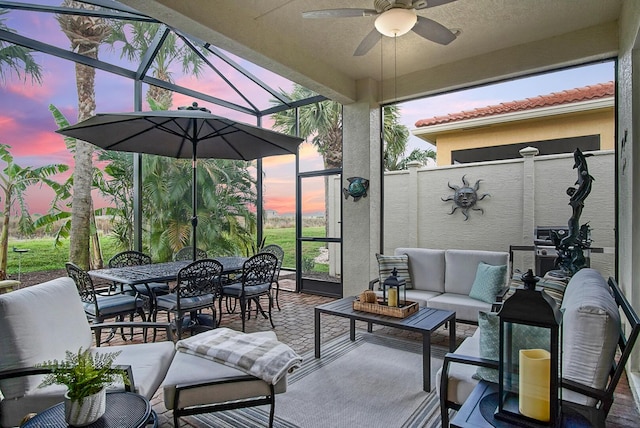 patio terrace at dusk featuring outdoor dining area, a ceiling fan, a lanai, and outdoor lounge area