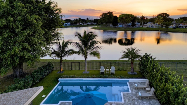 pool at dusk with a water view and a lawn