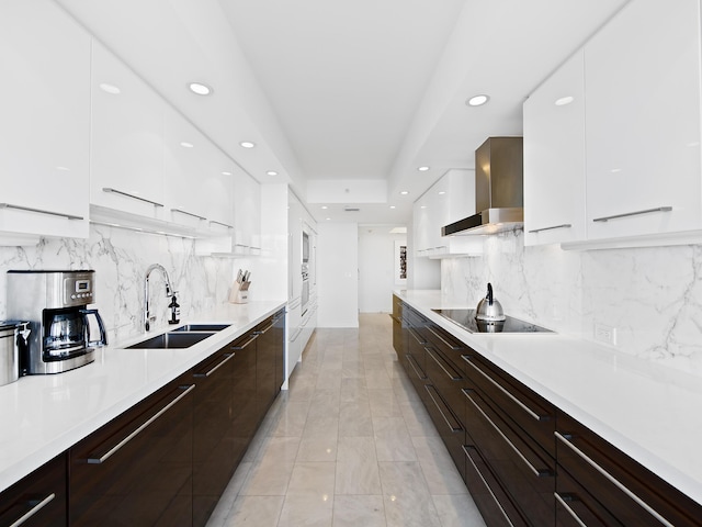 kitchen with black electric cooktop, sink, white cabinets, and wall chimney range hood