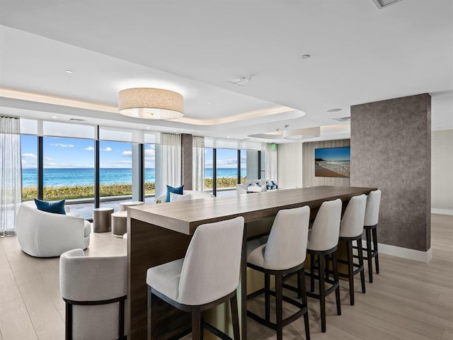 kitchen featuring a tray ceiling, a water view, a kitchen breakfast bar, and light hardwood / wood-style floors