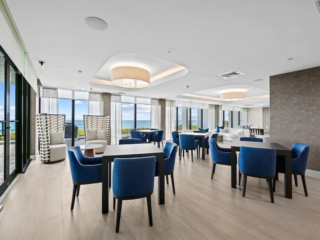 dining room featuring a wall of windows, a water view, a tray ceiling, and light wood-type flooring