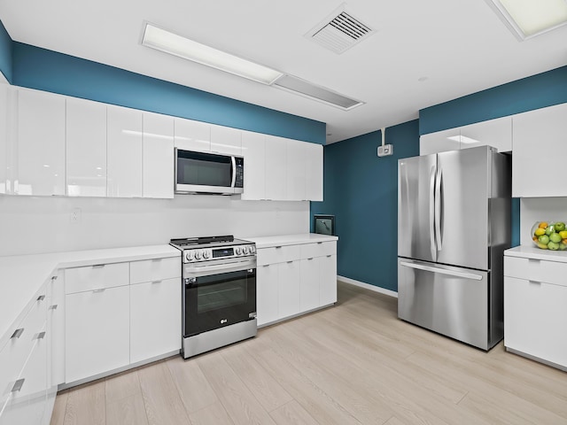 kitchen with white cabinets, appliances with stainless steel finishes, and light hardwood / wood-style flooring