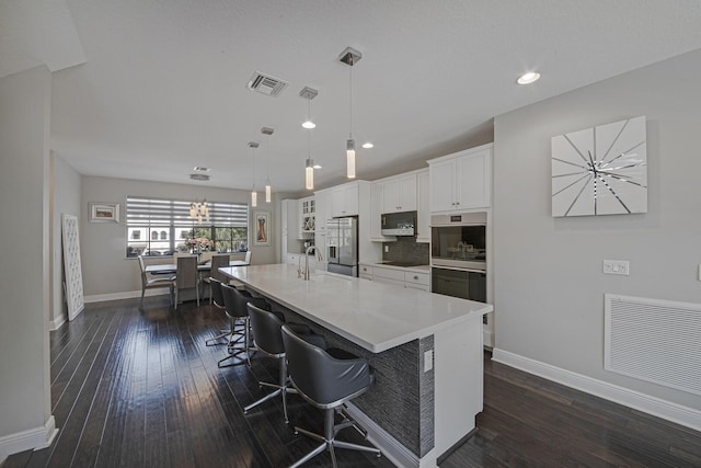 kitchen with dark wood-style flooring, visible vents, stainless steel double oven, white cabinets, and a sink