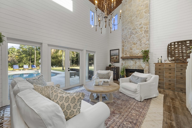 living room with a notable chandelier, a stone fireplace, a towering ceiling, and hardwood / wood-style flooring