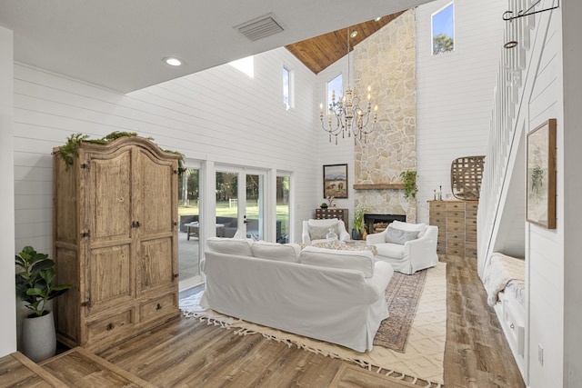 living room featuring a stone fireplace, a towering ceiling, hardwood / wood-style floors, wooden walls, and a chandelier